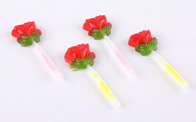 La fluorescencia enciende para arriba la piruleta de la forma de la flor de Rose del caramelo con el palillo de la iluminación